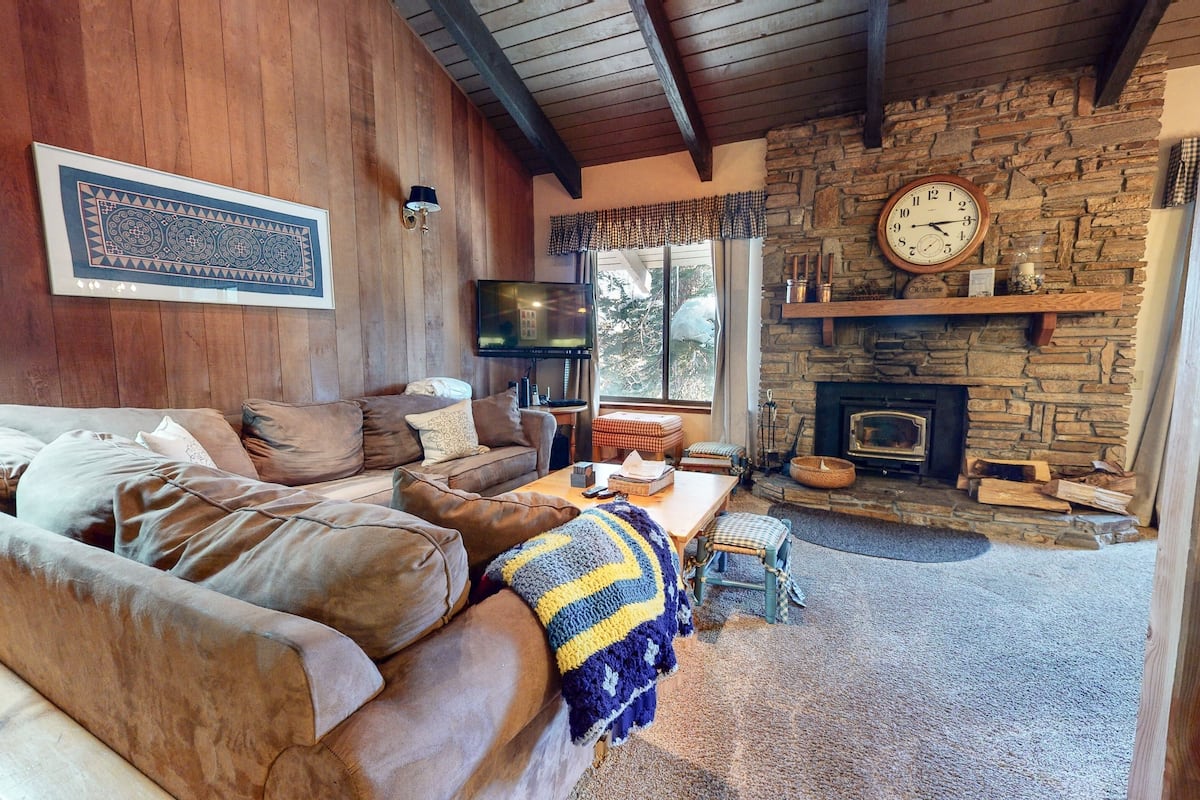 A cozy living room with a stone fireplace, wooden walls, and a comfortable seating area.