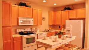 A kitchen with wooden cabinets, a microwave, stove, refrigerator, and a table with tea set. - Shv1168ha - 4 Bedroom Townhome In Coral Cay Resort, Sleeps Up To 10, Just 6 Miles To Disney (Kissimmee)