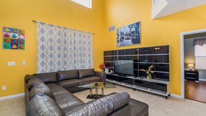 A living room with a sectional sofa, a flat-screen TV, and a patterned curtain.