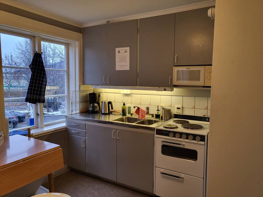 Een kleine keuken met grijze kastjes, een magnetron, een fornuis en een raam met uitzicht.