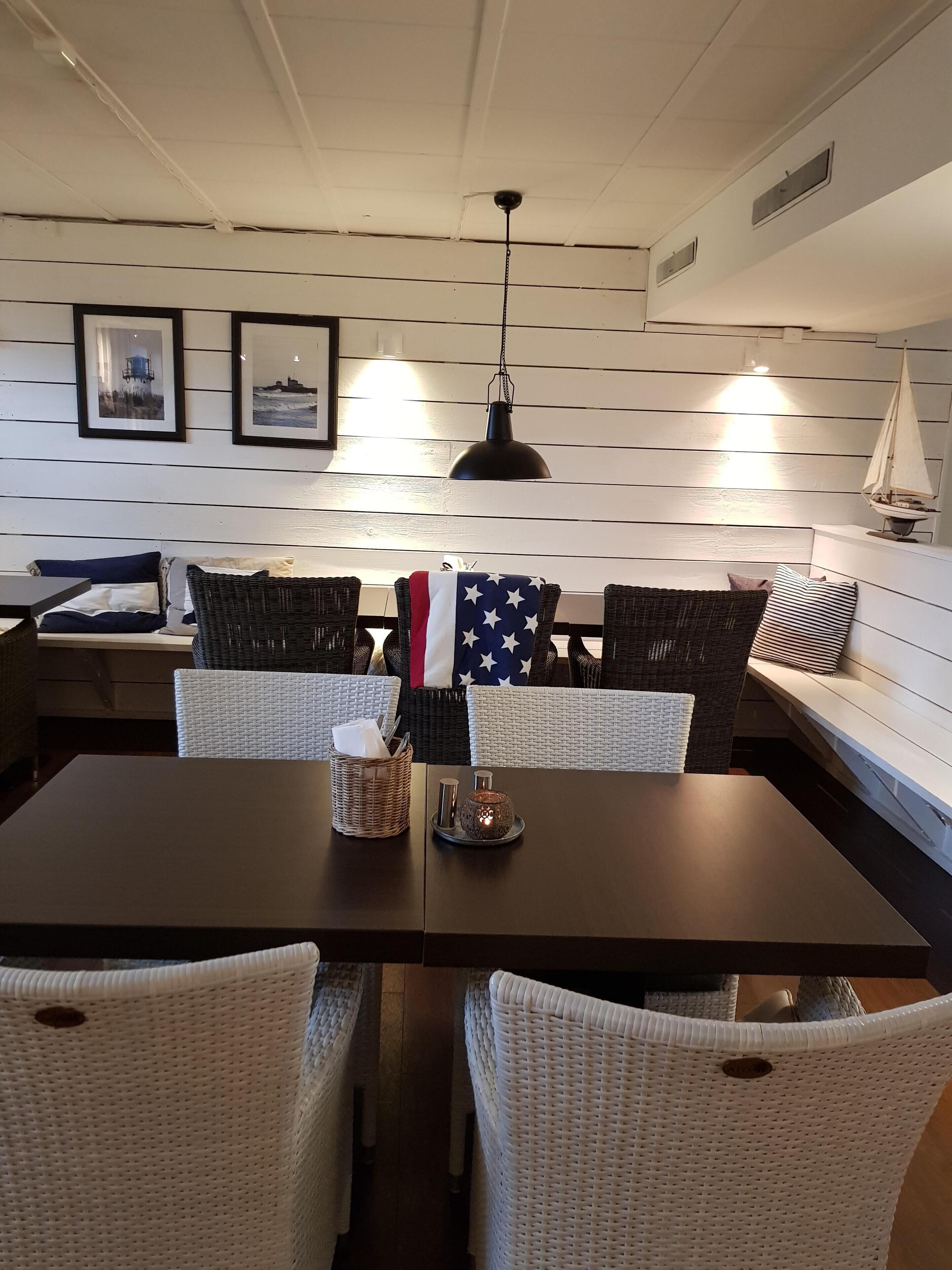 Un comedor con una mesa de madera oscura, sillas de mimbre blanco y un banco con cojines a rayas. Hay cuadros en la pared y una pequeña decoración con forma de velero.