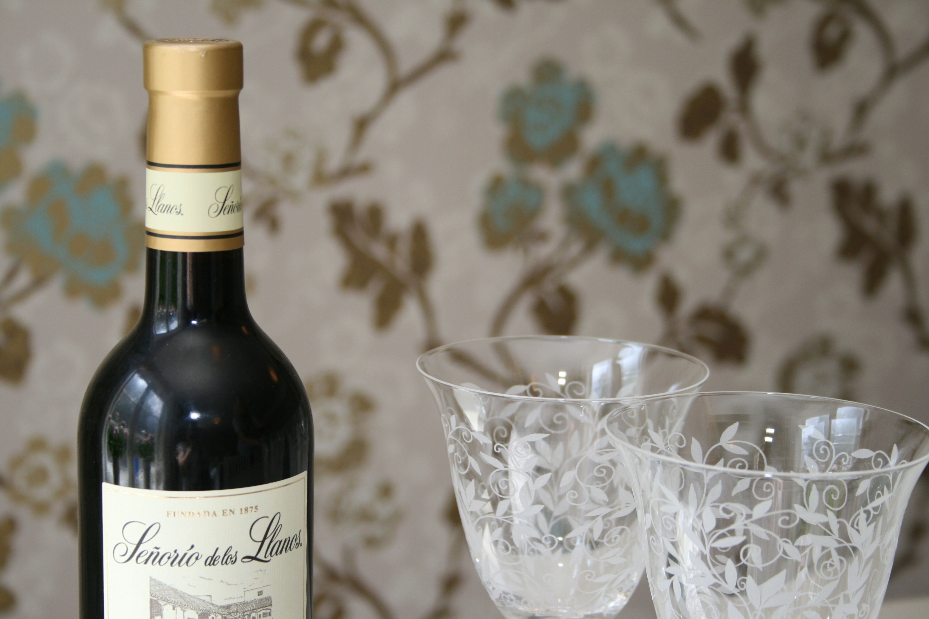 Uma garrafa de vinho com etiqueta e duas taças de vidro ricamente decoradas.