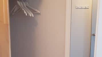 A small, white room with a wooden shelf, a mirror, and a white table.