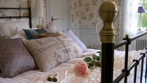 A neatly made bed with a floral-patterned headboard, a decorative pillow, a rose, and a pair of slippers.