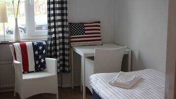 Un dormitorio con cama, una silla, un escritorio y una ventana con cortinas.