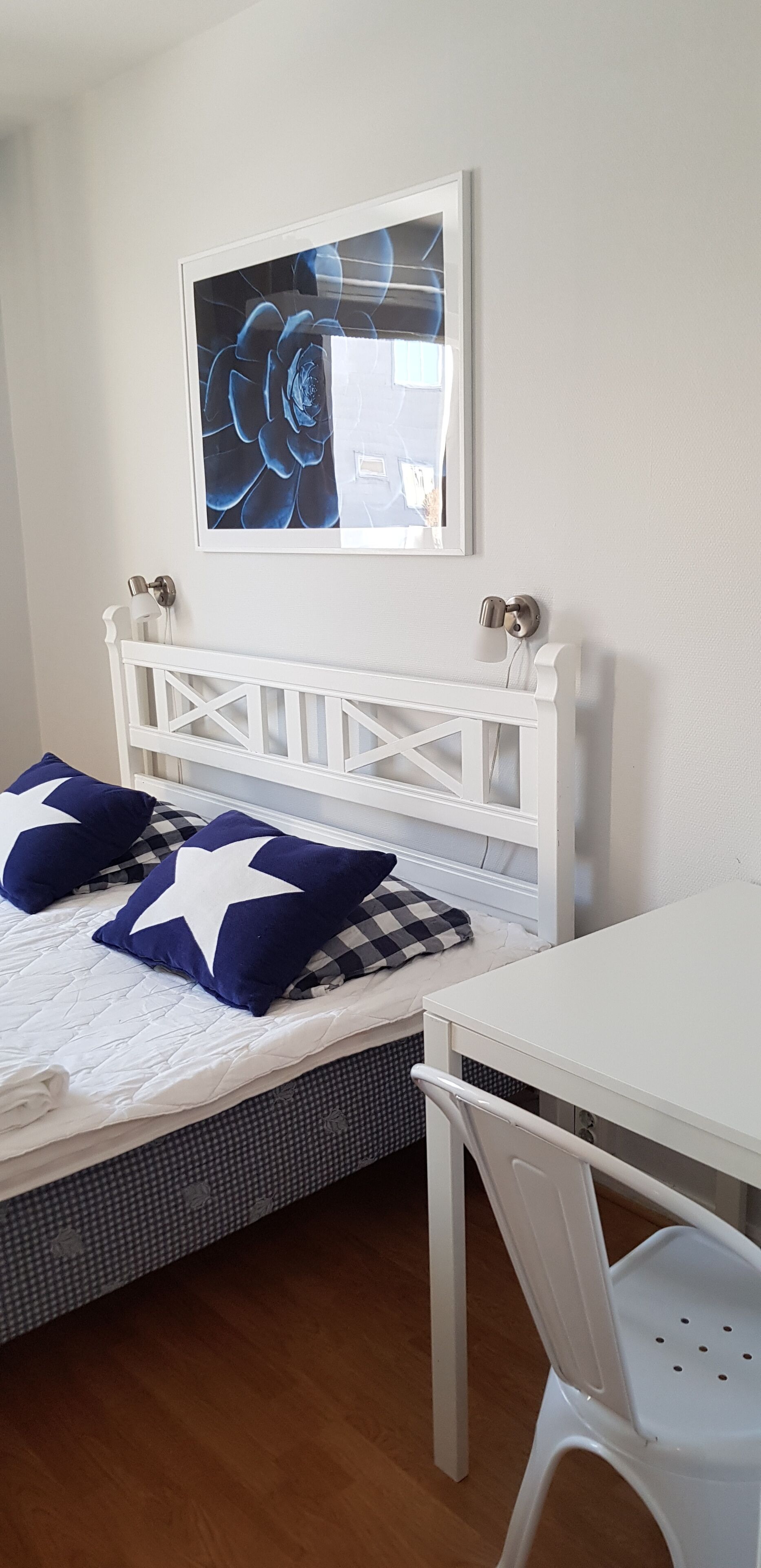 Ein Schlafzimmer mit einem weißen Bett, einem weißen Schreibtisch und einem an der Wand hängenden Bild.
