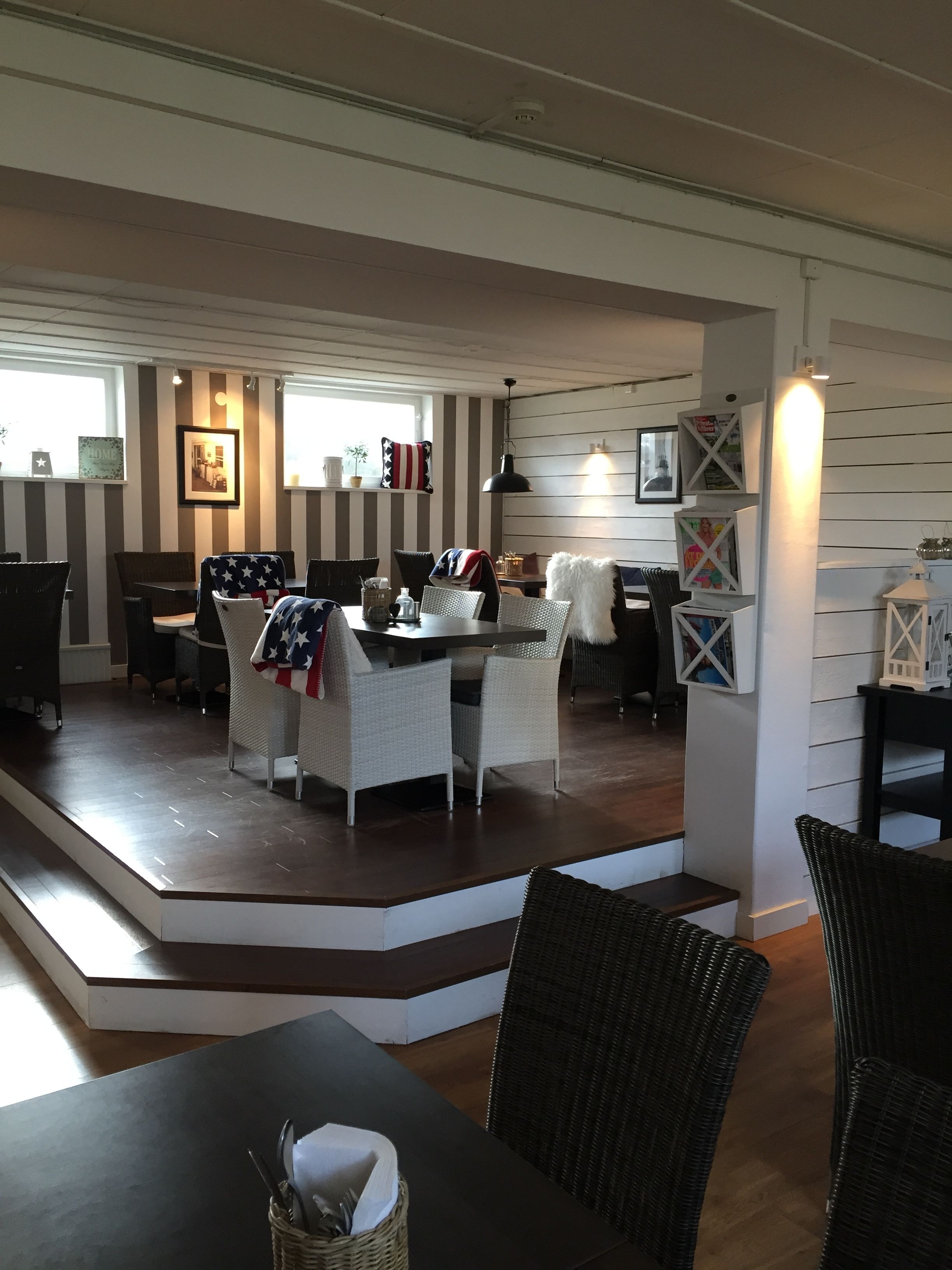 A dining area with a long table and wicker chairs, a staircase leading to another level, and a wall with striped panels and framed pictures.