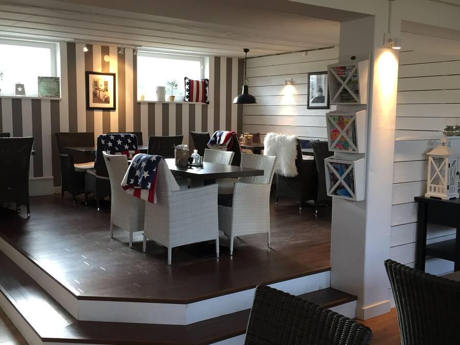 A dining area with a long table and wicker chairs, a staircase leading to another level, and a wall with striped panels and framed pictures.