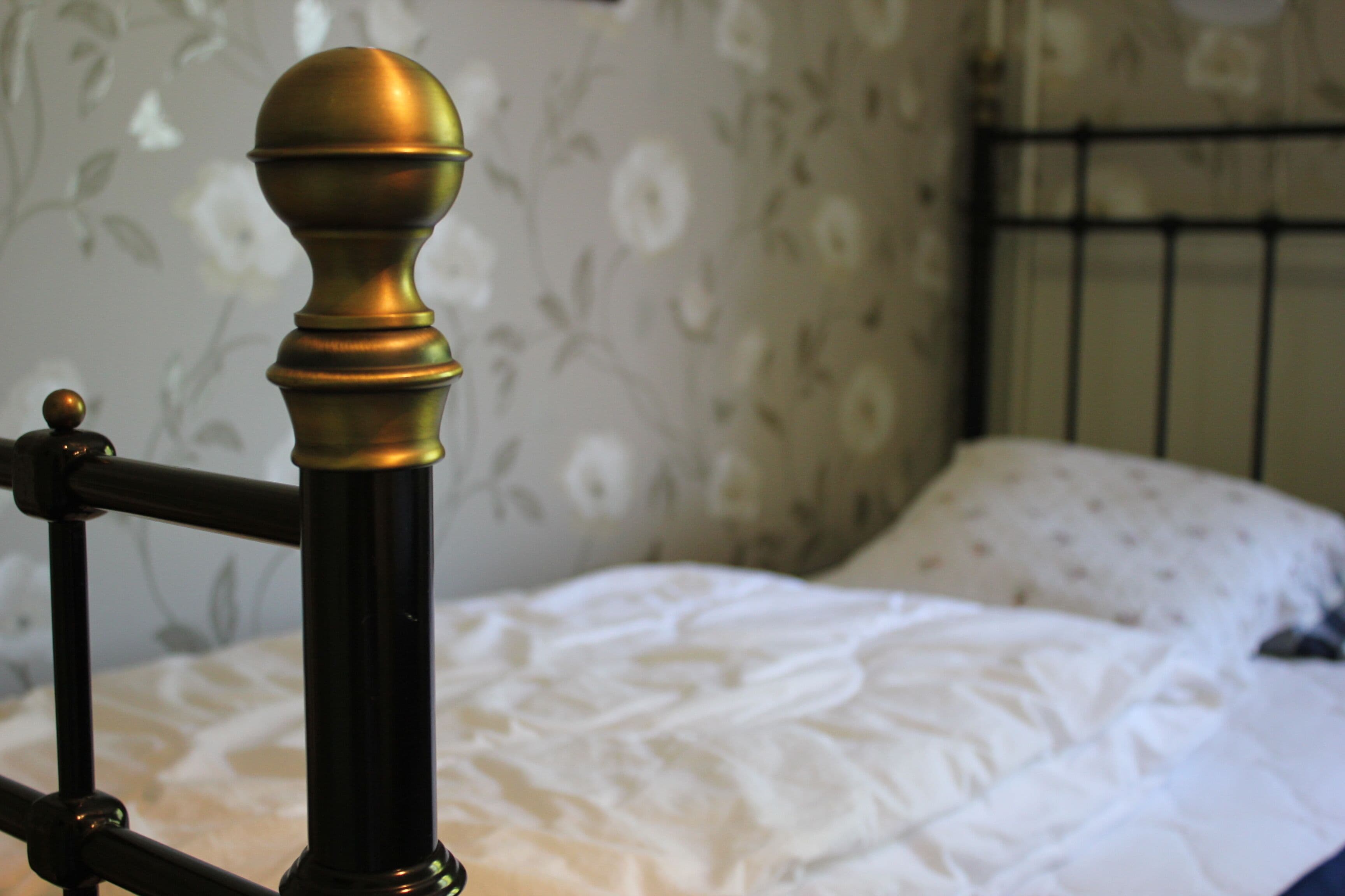 A bed with a white bedspread and a metal headboard with a decorative finial.