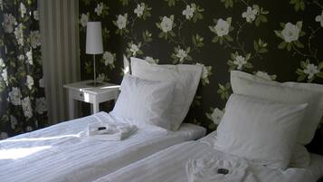 A hotel room with two beds, white linens, a nightstand with a lamp, and floral wallpaper.