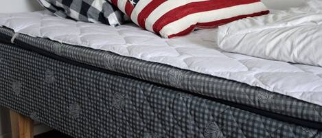 Una cama con cabecera acolchada, almohada de cuadros y almohada con la bandera estadounidense.