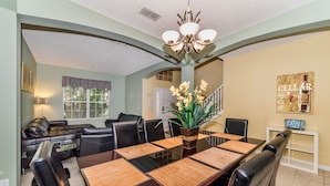 A dining area with a long table, chairs, a chandelier, and a staircase in the background. - Emerald Island #2 - 7 Bed 5 Baths Villa (Kissimmee)
