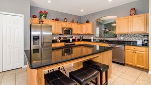 A modern kitchen with a central island, wooden cabinets, stainless steel appliances, and a black countertop. - Emerald Island #2 - 7 Bed 5 Baths Villa (Kissimmee)