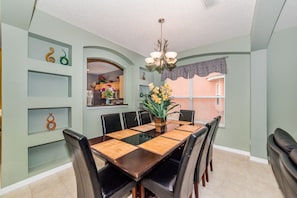 A dining area with a long table, chairs, and a chandelier. - Emerald Island #2 - 7 Bed 5 Baths Villa (Kissimmee)