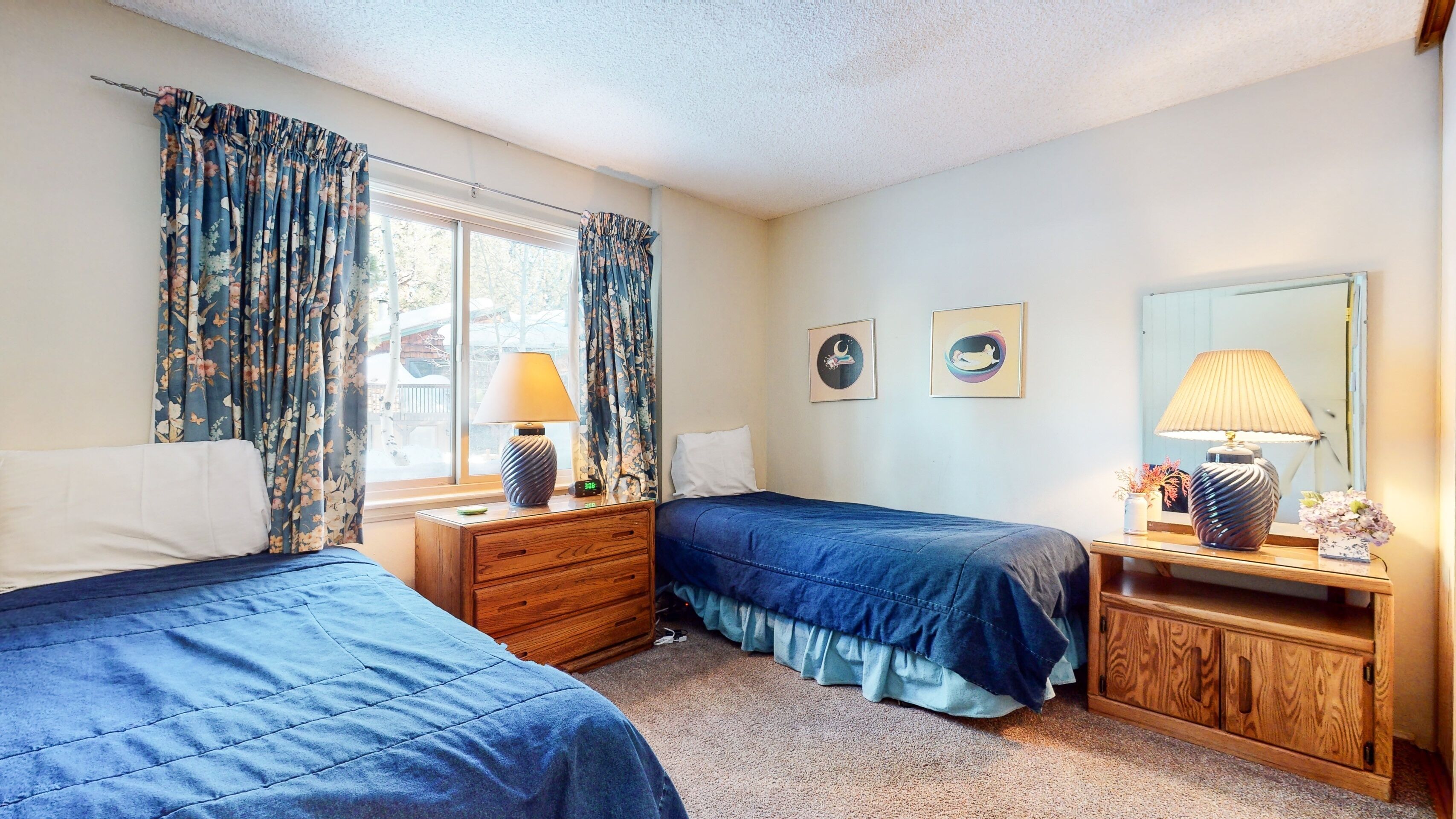 A bedroom with two beds, a wooden dresser, a nightstand, and a window with curtains.