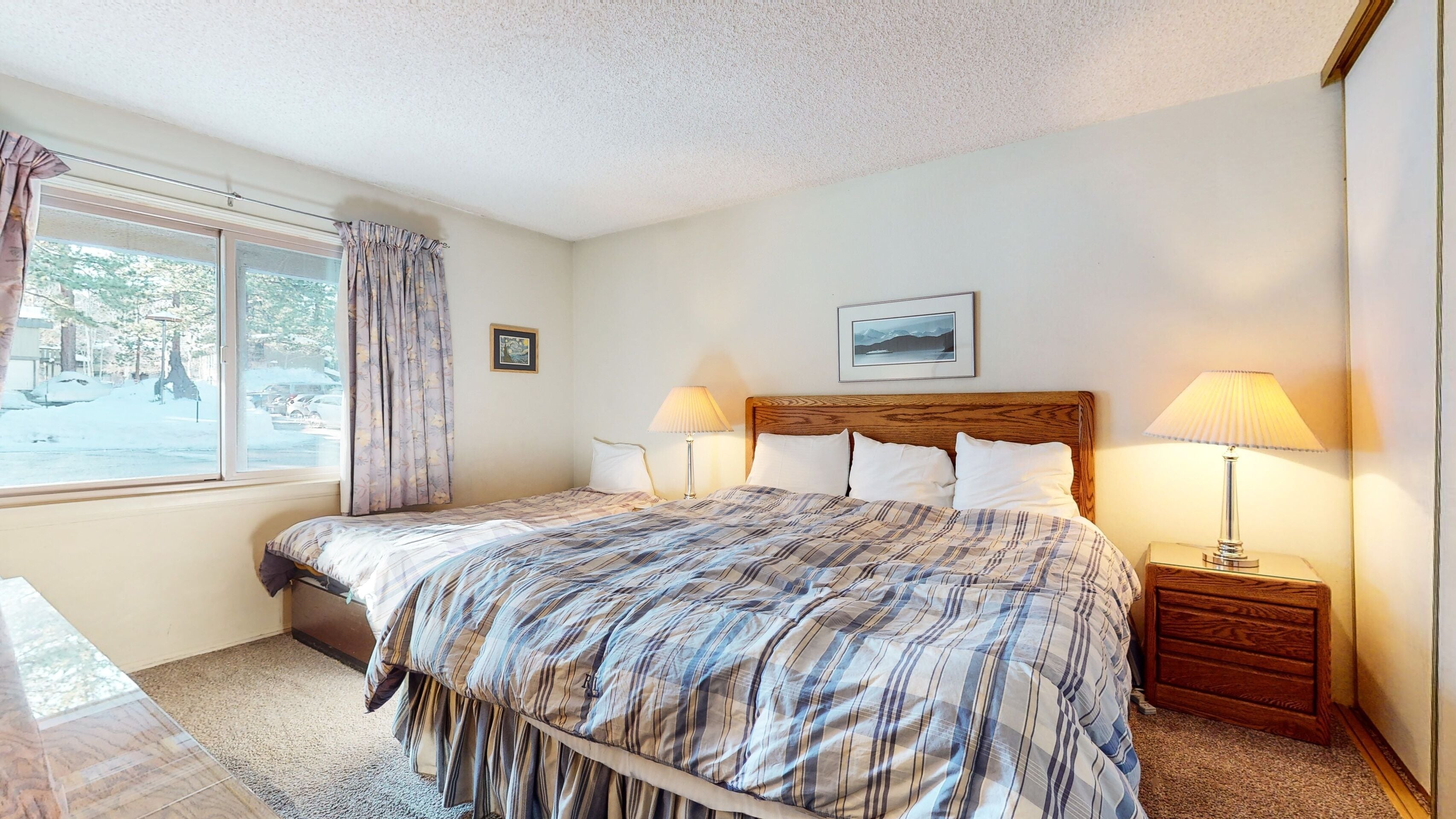 A neatly arranged bedroom with a large bed, two bedside lamps, a framed picture on the wall, and a window with curtains.