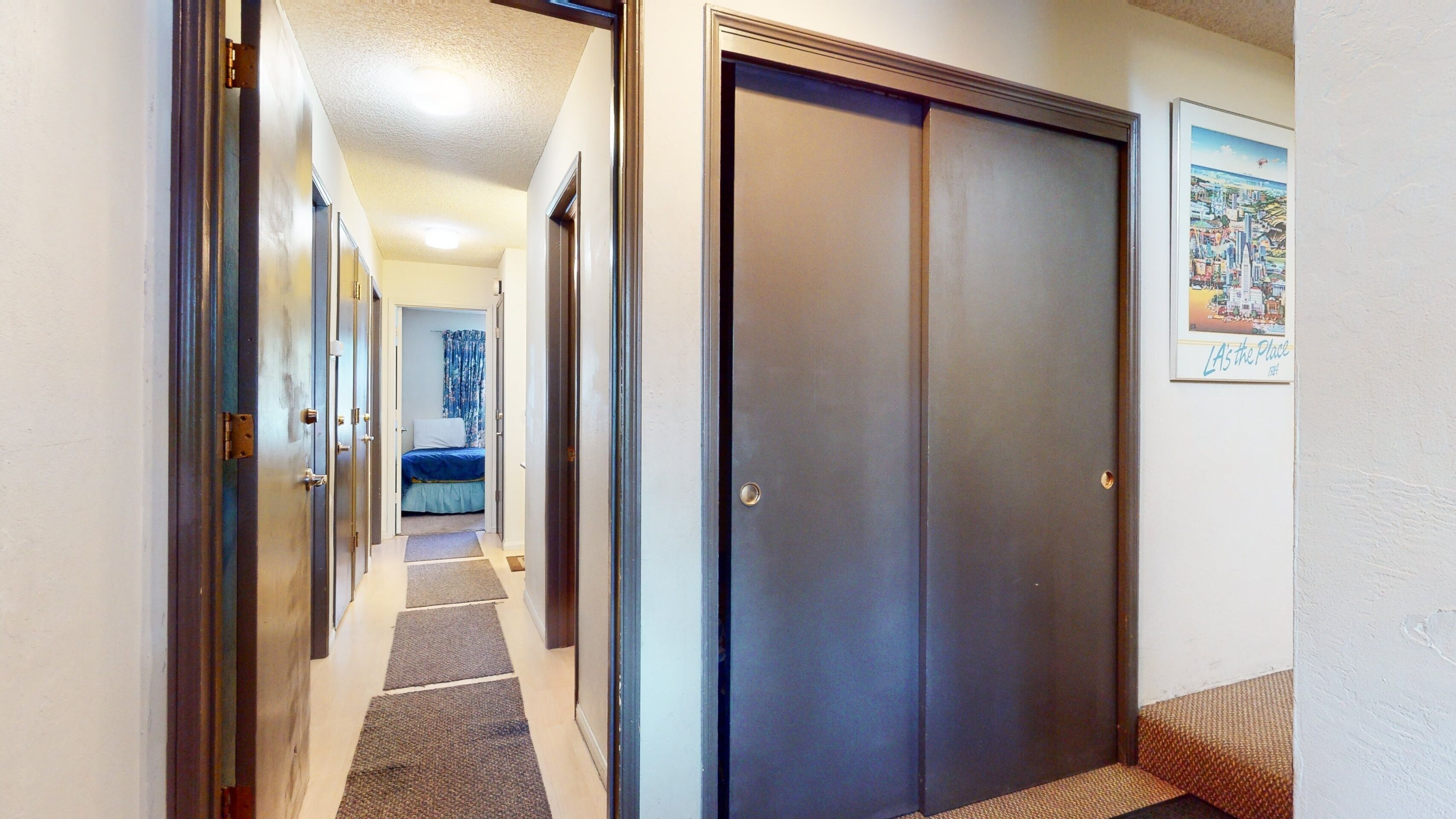 A hallway leading to a bedroom with a bed, a door, and a framed picture on the wall.