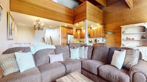 A cozy living room with a sectional sofa, wooden ceiling beams, and a kitchen in the background. - Bridges Townhome 7 Gorgeous Mountain Views, Private Jacuzzi, Steps to Eagle Lodge by RedAwning (Mammoth Lakes)