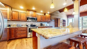 A kitchen with wooden cabinets, stainless steel appliances, granite countertops, and a large island with stools. - Bridges Townhome 7 Gorgeous Mountain Views, Private Jacuzzi, Steps to Eagle Lodge by RedAwning (Mammoth Lakes)