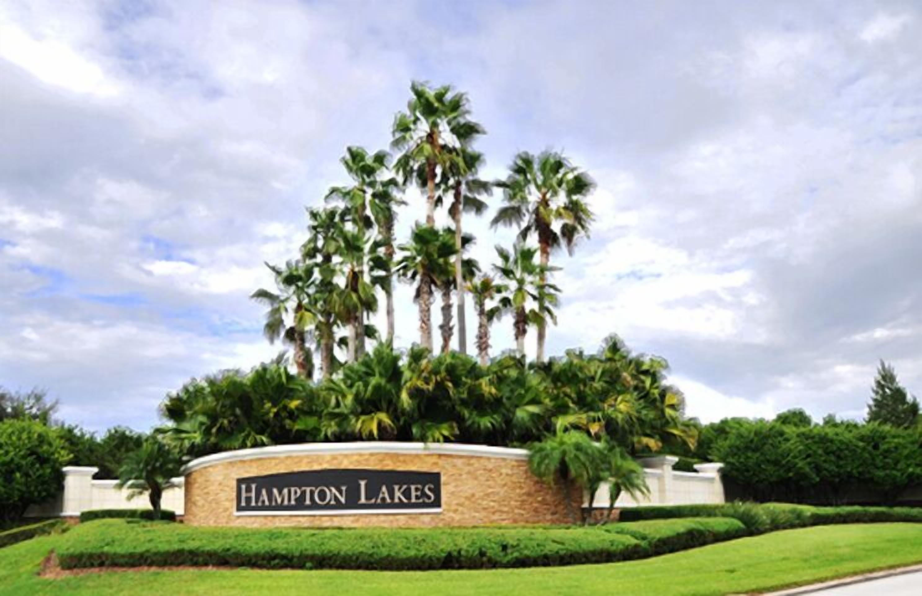 Naamplaatje voor Hampton Lakes, met een aangelegde omgeving met palmbomen en goed onderhouden gras.