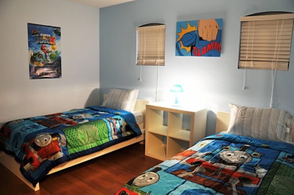 Un dormitorio con dos camas individuales, cada una con una colcha temática de Thomas el Tren. Hay dos mesitas de noche, una con lámpara, y un cartel en la pared.
