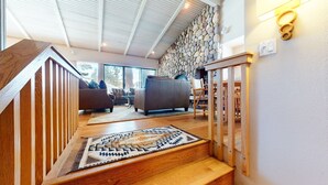 A staircase with wooden railings leading to a living area with a stone wall and a fireplace. - Mammoth West 137 Updated Deluxe Condo, Just A Short Walk to Canyon Lodge by RedAwning (Mammoth Lakes)