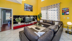 A living room with a sectional sofa, a flat-screen TV, a glass coffee table, and a potted plant.