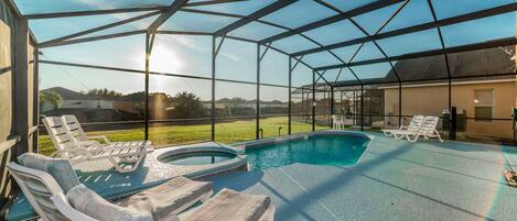 A covered outdoor swimming pool area with lounge chairs and a hot tub.