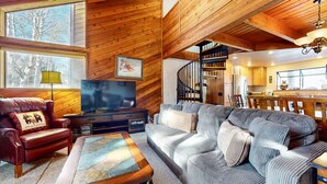 A cozy living room with a leather sofa, a television, and a wooden staircase leading to a kitchen. - Snowflower 26 Remodeled Spacious Condo With Great Complex Amenities by RedAwning (Mammoth Lakes)