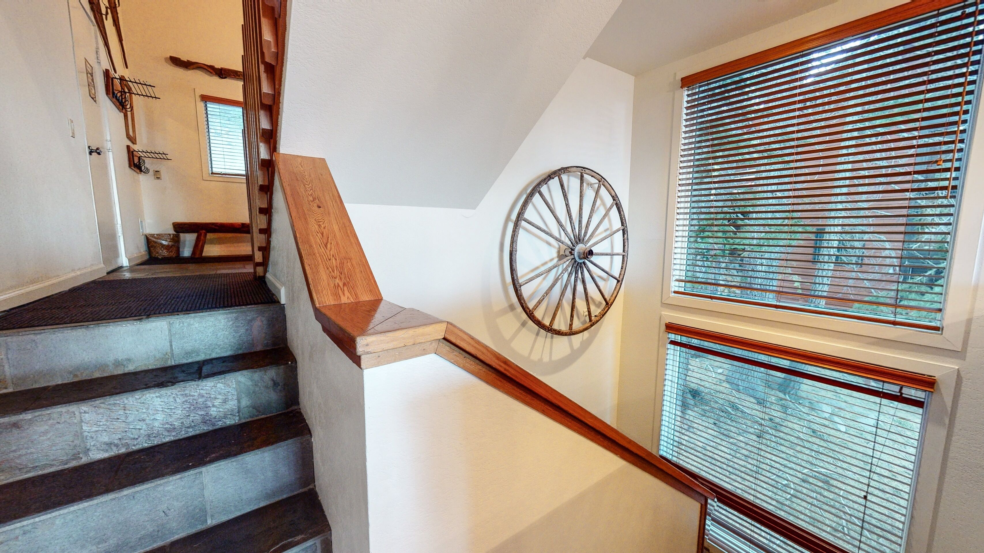 Una escalera de madera con peldaños y barandilla, que conduce a una plataforma con una rueda decorativa grande.