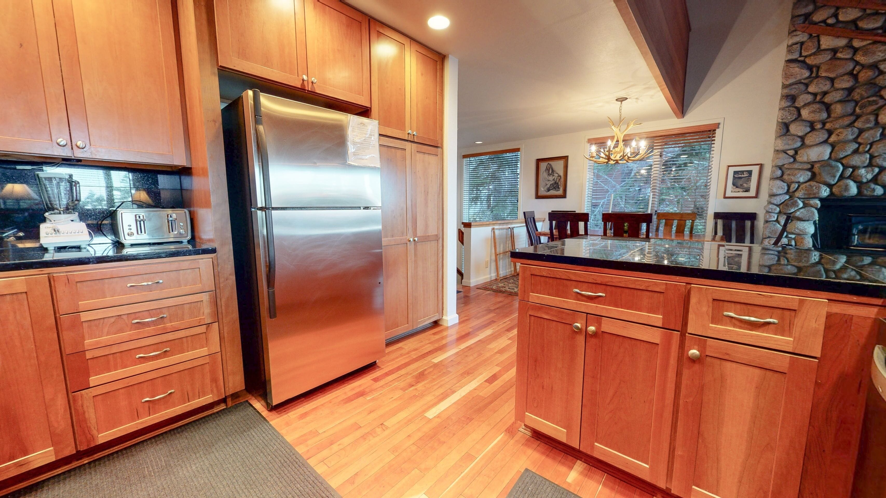 A modern kitchen with wooden cabinets, a stainless steel refrigerator, and a stone accent wall.