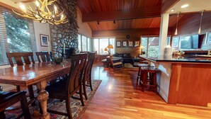 Un comedor espacioso con una mesa y sillas de madera, una chimenea de piedra y vistas al exterior a través de amplios ventanales.