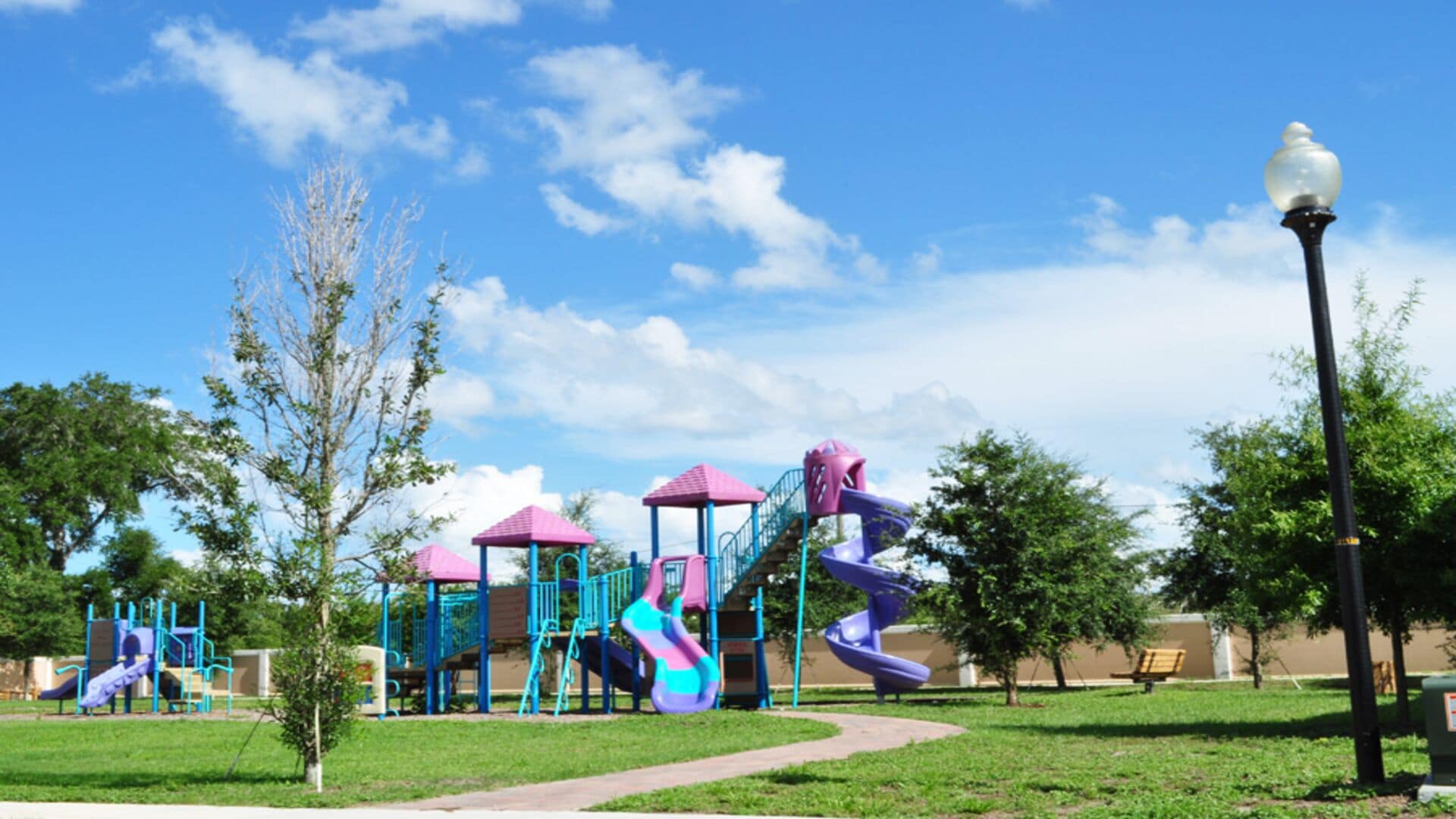 A playground with slides and climbing structures, surrounded by grass and trees.