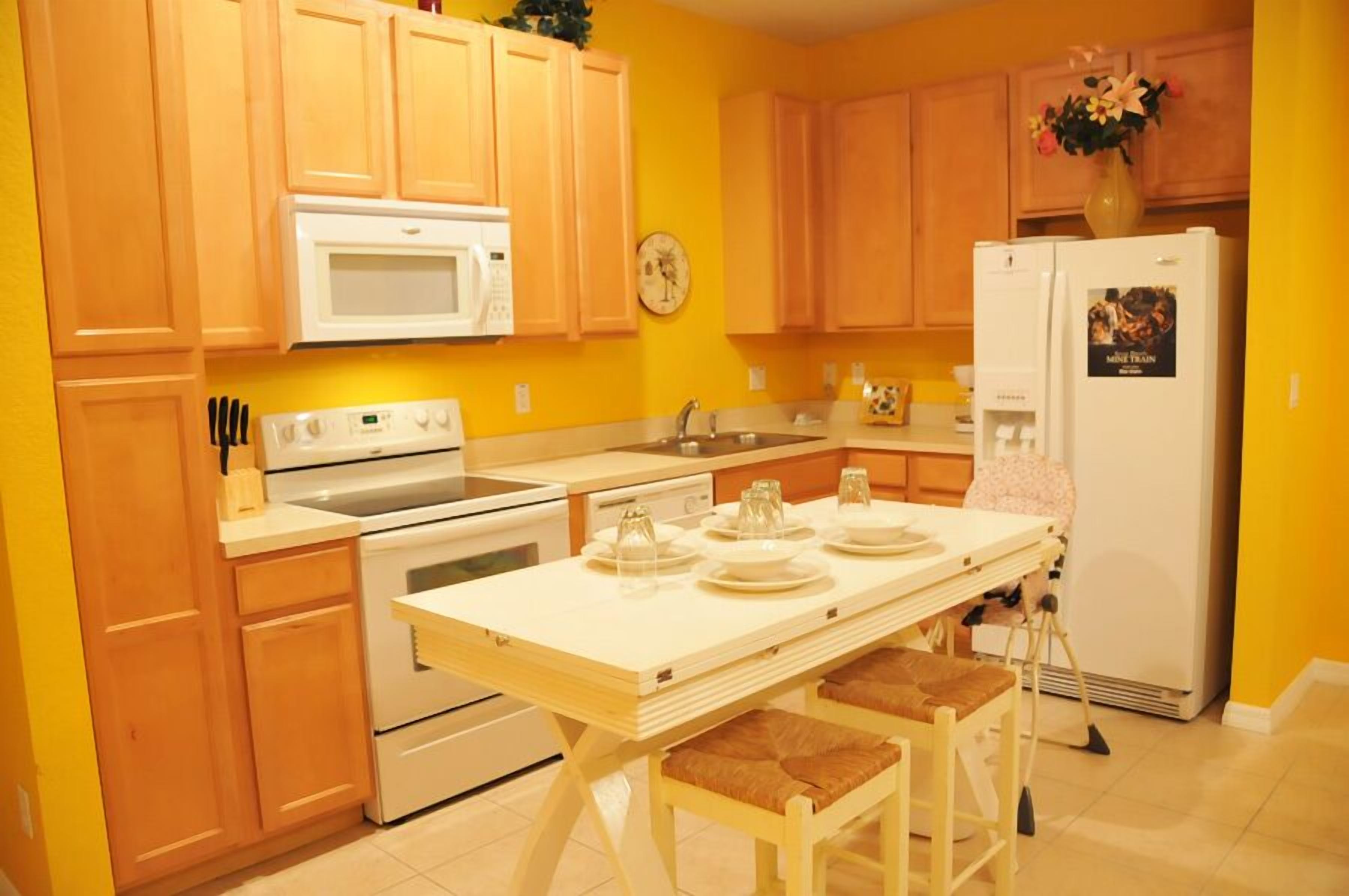 Une cuisine avec des meubles en bois, un micro-ondes blanc, une cuisinière, un évier et une table à manger avec des chaises.