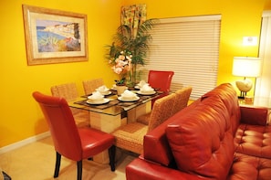 A dining area with a glass table, red chairs, a red sofa, and a painting on the wall. - Shv1172ha - 4 Bedroom Townhome In Coral Cay Resort, Sleeps Up To 8, Just 6 Miles To Disney (Kissimmee)