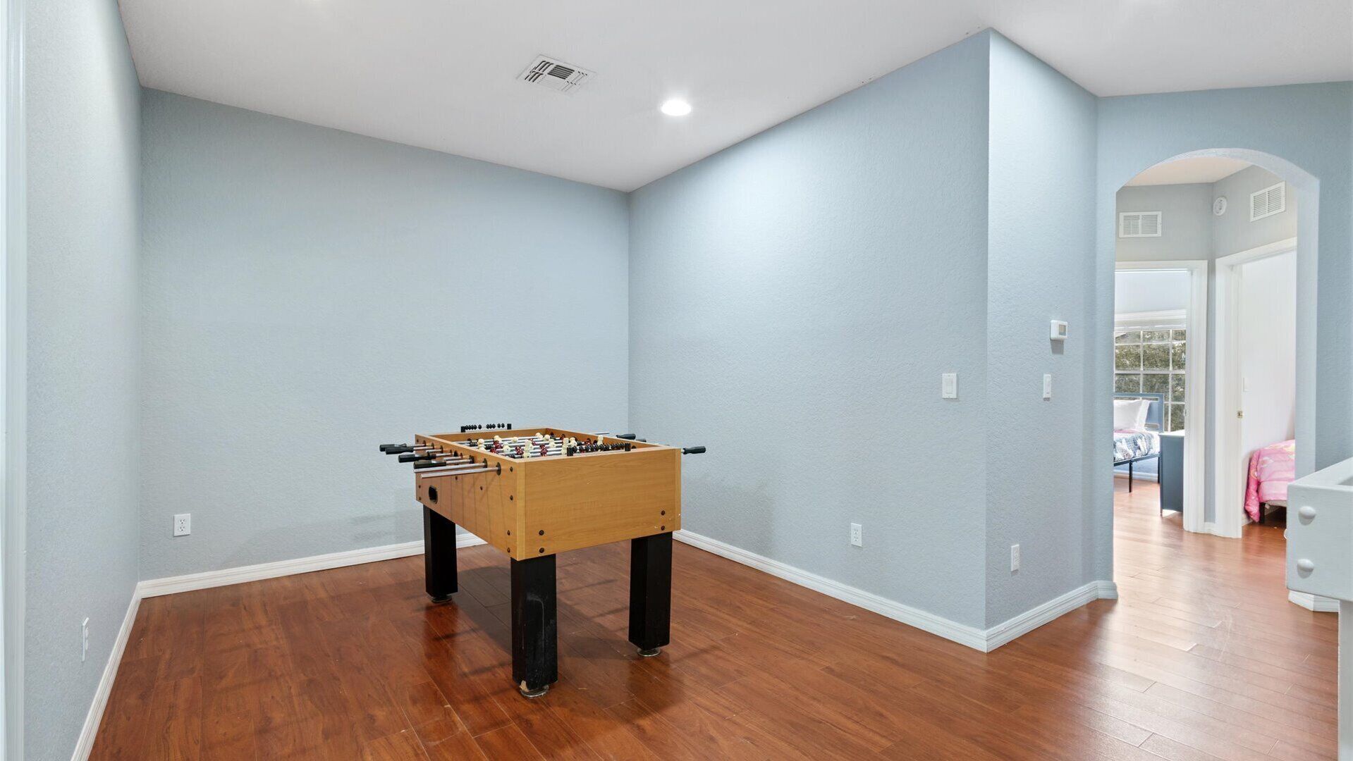 A room with a wooden foosball table, light blue walls, and hardwood flooring.