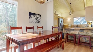 A dining area with a wooden table and chairs, a stone fireplace, and a kitchen with a stone countertop. - Mammoth West 115 Updated Condo, Just A Short Walk To Canyon Lodge by RedAwning (Mammoth Lakes)