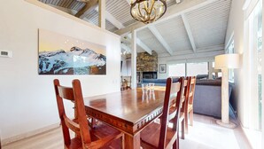 A spacious dining area with a wooden table and chairs, a stone fireplace, and a large painting of a mountain landscape on the wall. - Mammoth West 115 Updated Condo, Just A Short Walk To Canyon Lodge by RedAwning (Mammoth Lakes)