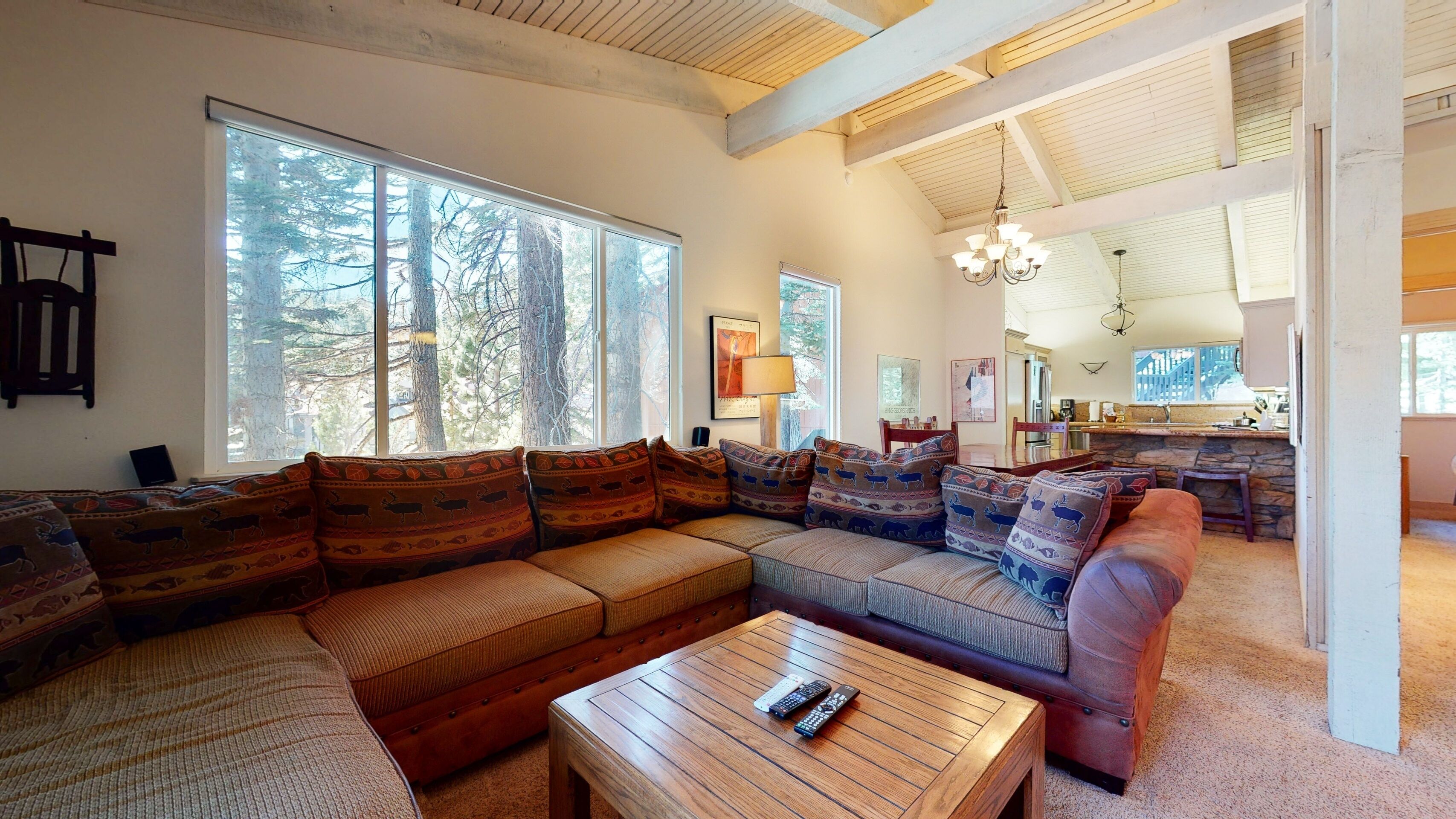 A spacious living room with a large sectional sofa, a wooden coffee table, and a view of the forest through large windows.