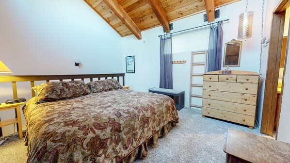 Un dormitorio con cama, cómoda, mesita de noche, lámpara y ventana con cortinas.