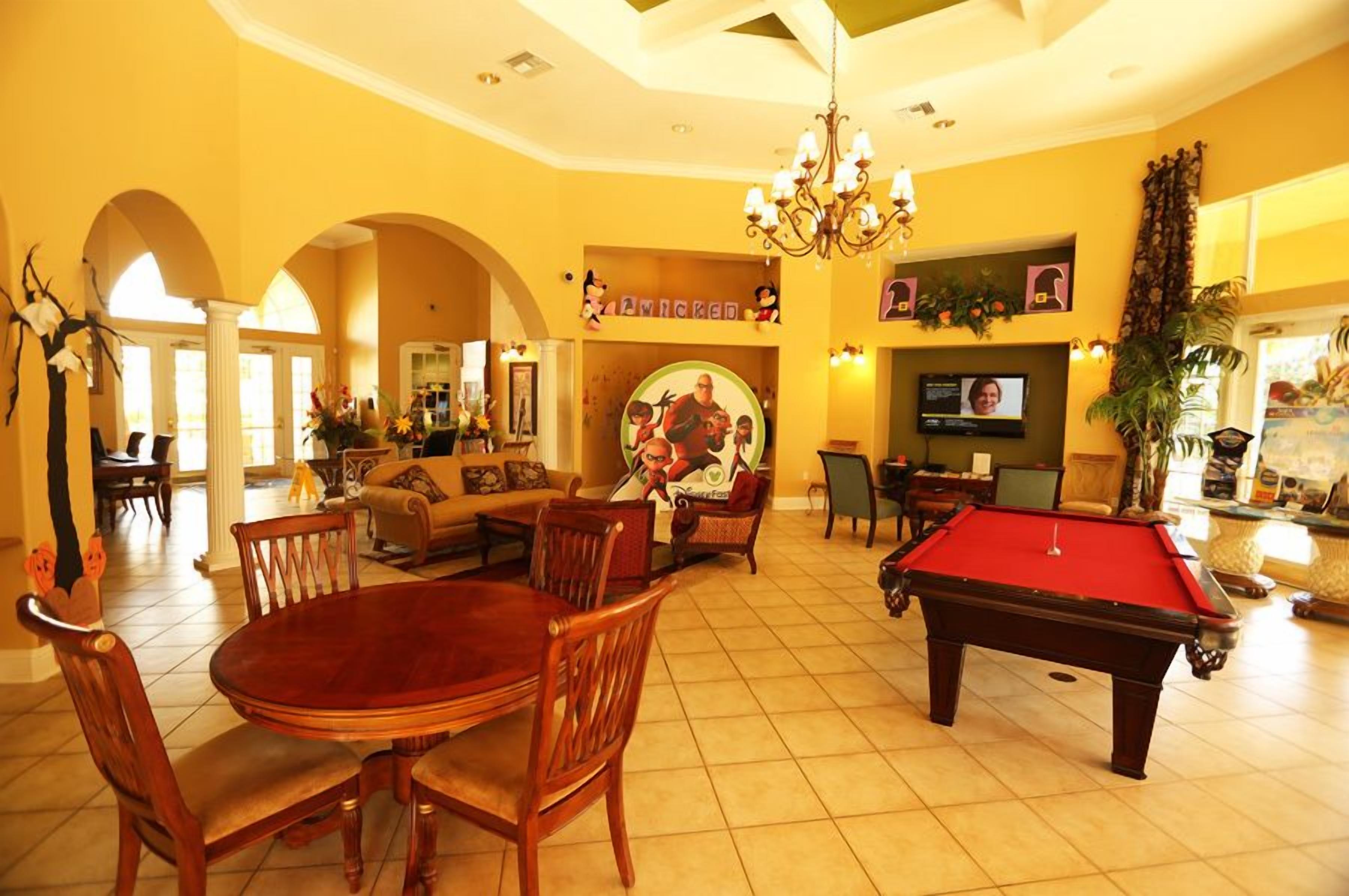 A spacious living room with a pool table, a billiards table, and a television. There are multiple seating areas, including a sofa and chairs.