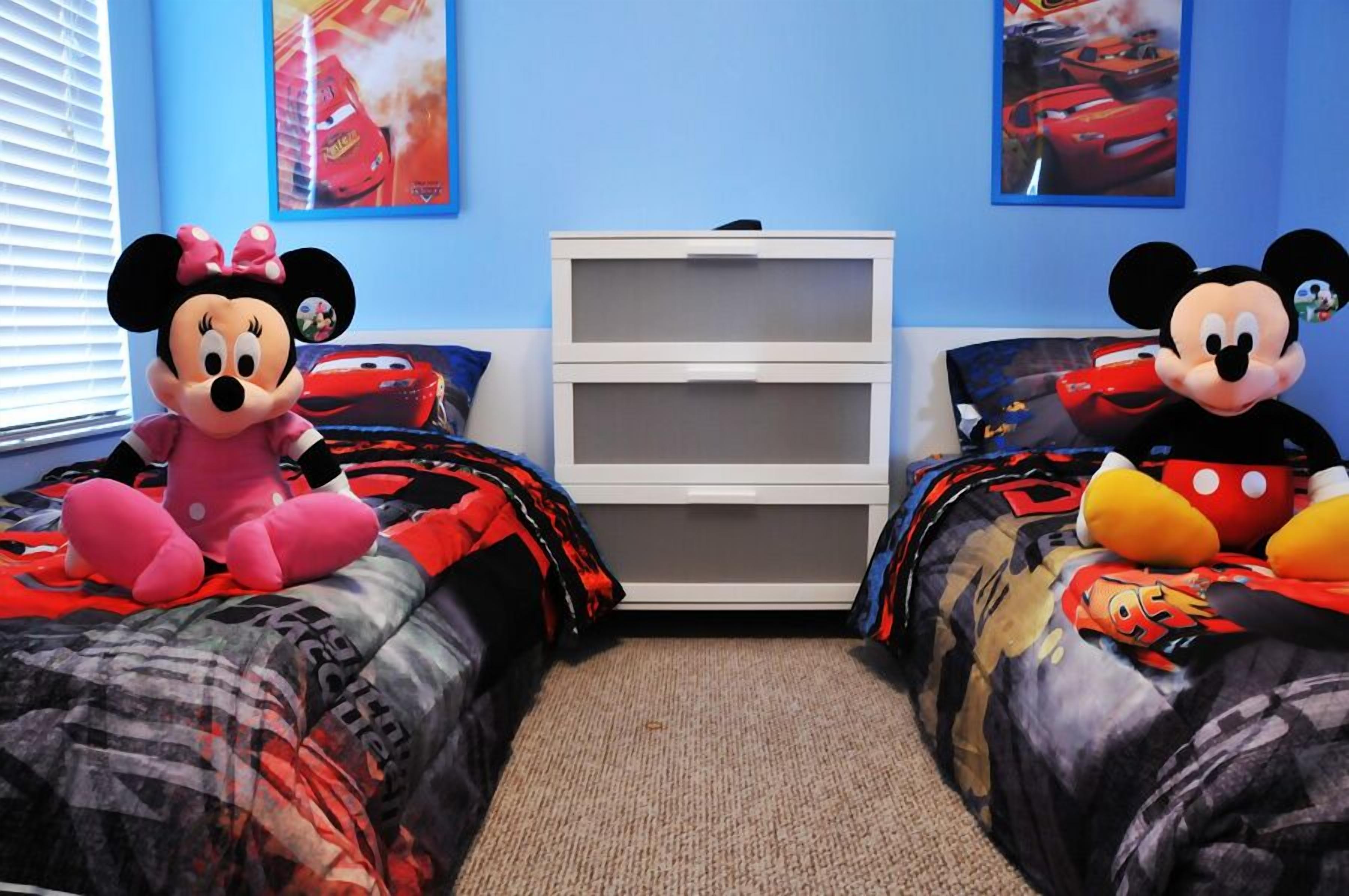 Een slaapkamer met twee bedden, elk voorzien van een Mickey Mouse knuffel, een witte dressoir en posters aan de muur.