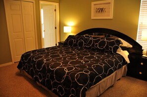 A bedroom with a bed, a nightstand, a lamp, a door, and a framed picture on the wall.