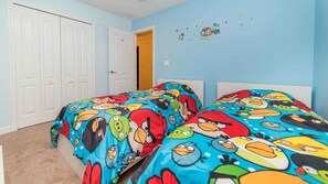 Un dormitorio con dos camas, cada una cubierta con un edredón de diseño colorido de Angry Birds. Se observa una puerta blanca y una pared azul claro con un pequeño adorno.