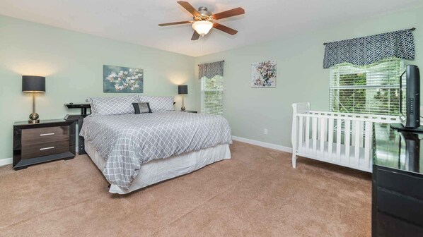 A bedroom with a bed, nightstands, a ceiling fan, a crib, and artwork on the walls.