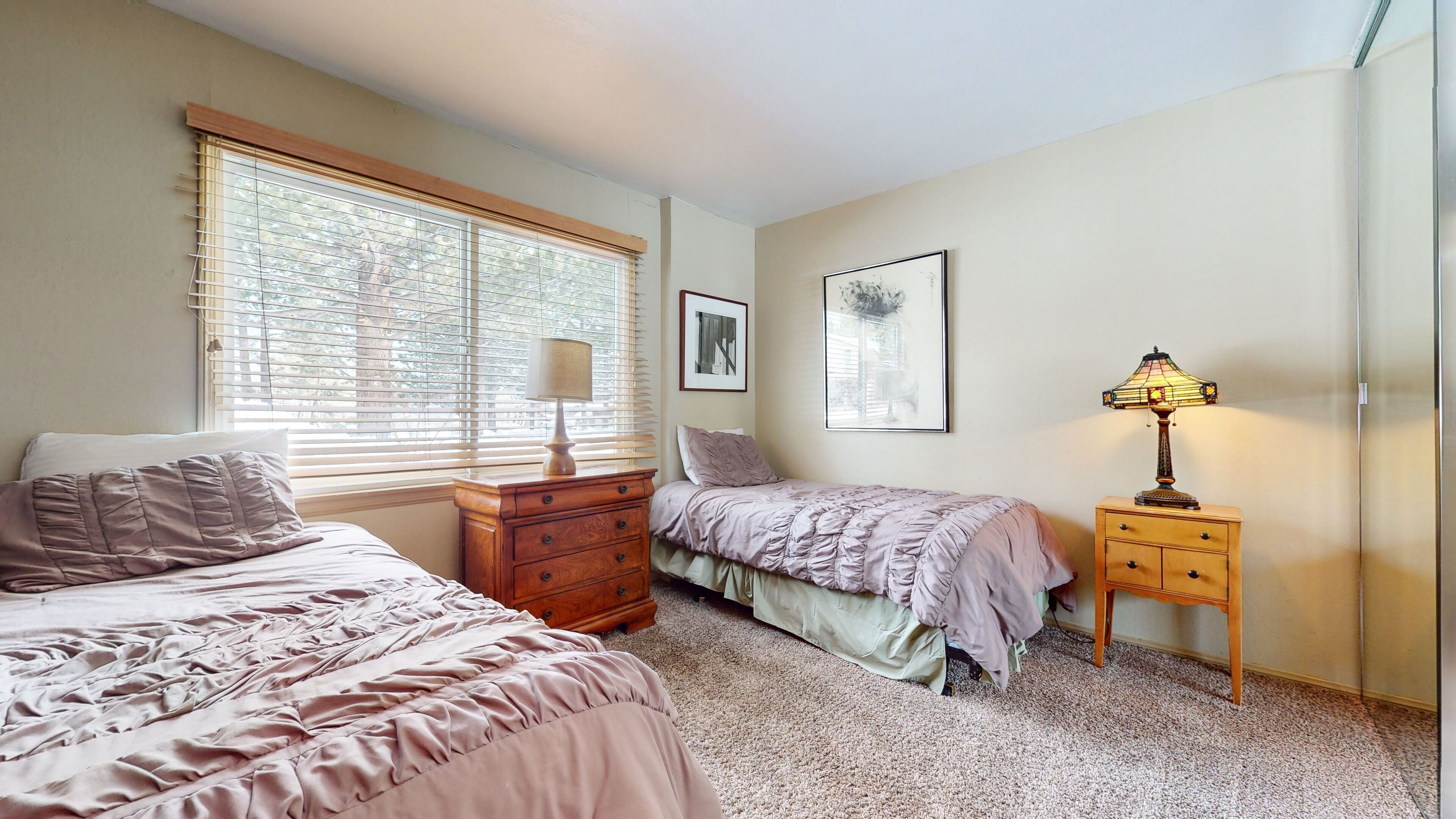 A bedroom with two beds, a dresser, a nightstand, and a window with blinds.