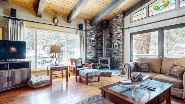 A cozy living room with a fireplace, wooden furniture, and large windows.