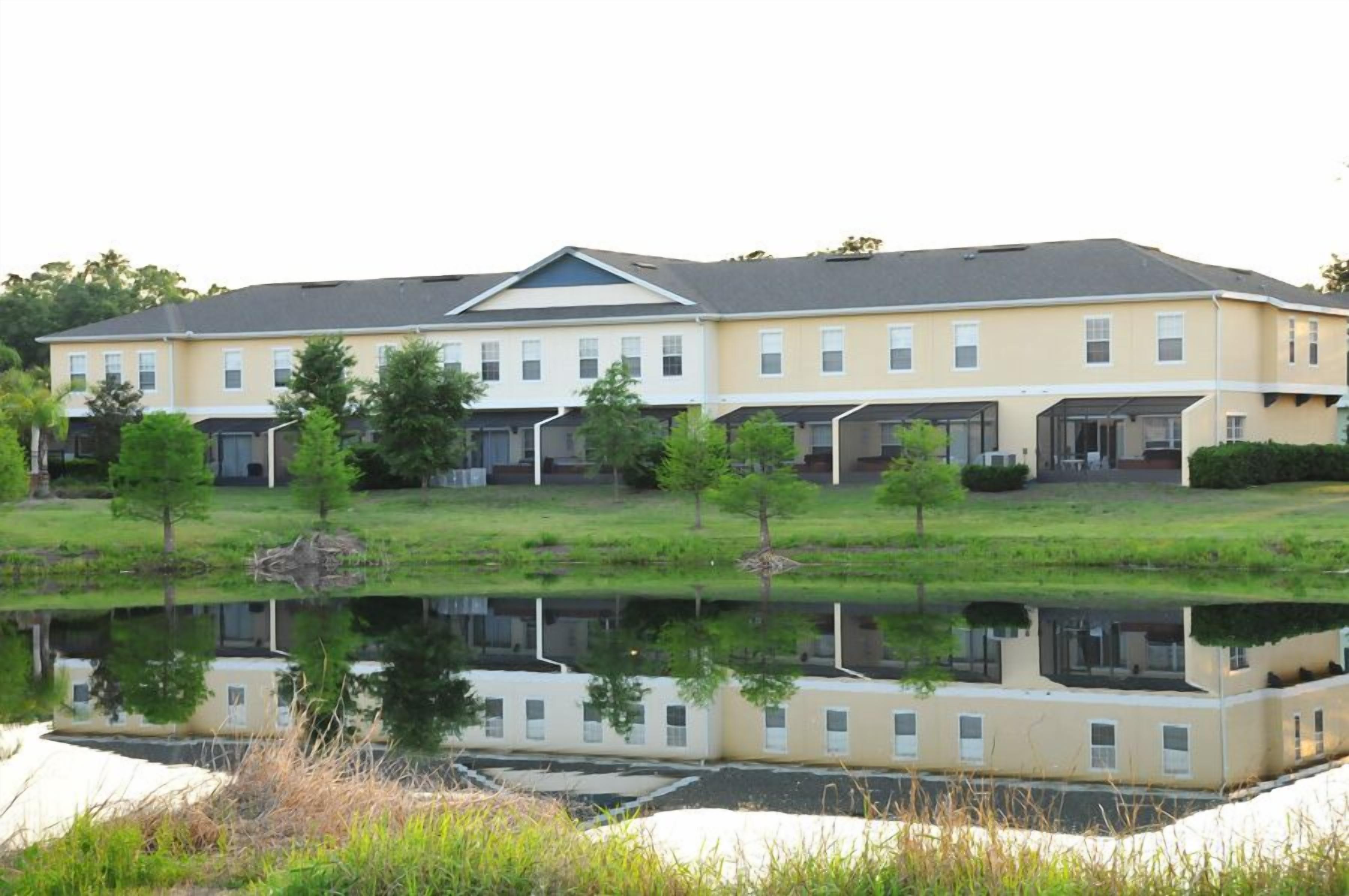 A multi-story hotel with a flat roof, large windows, and a reflection in a body of water.