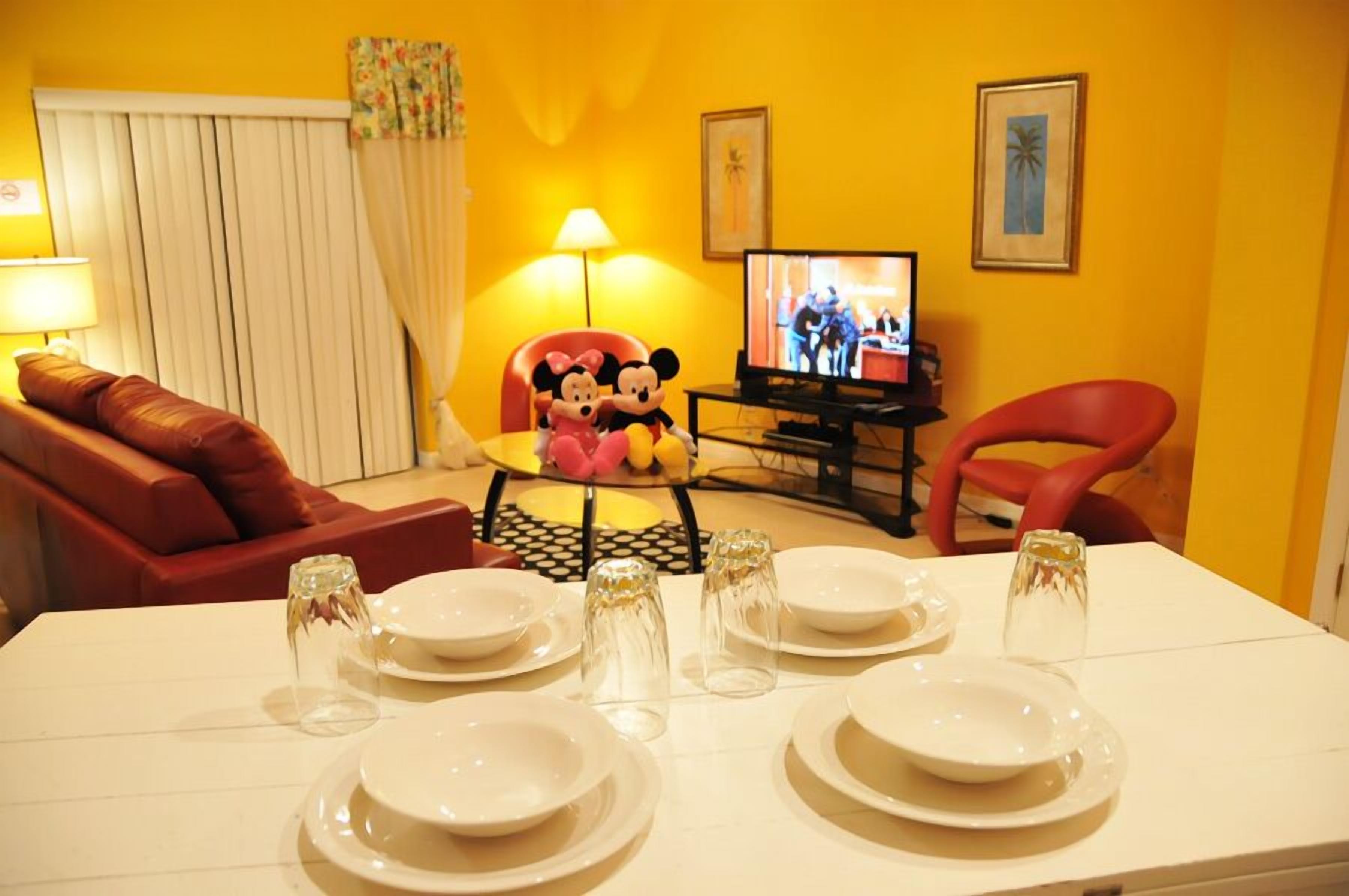 A dining area with a table set for four, a television, and a red chair.