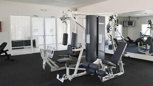 Ein Fitnessstudio mit verschiedenen Trainingsgeräten, einem großen Spiegel und einem Fernseher an der Wand.